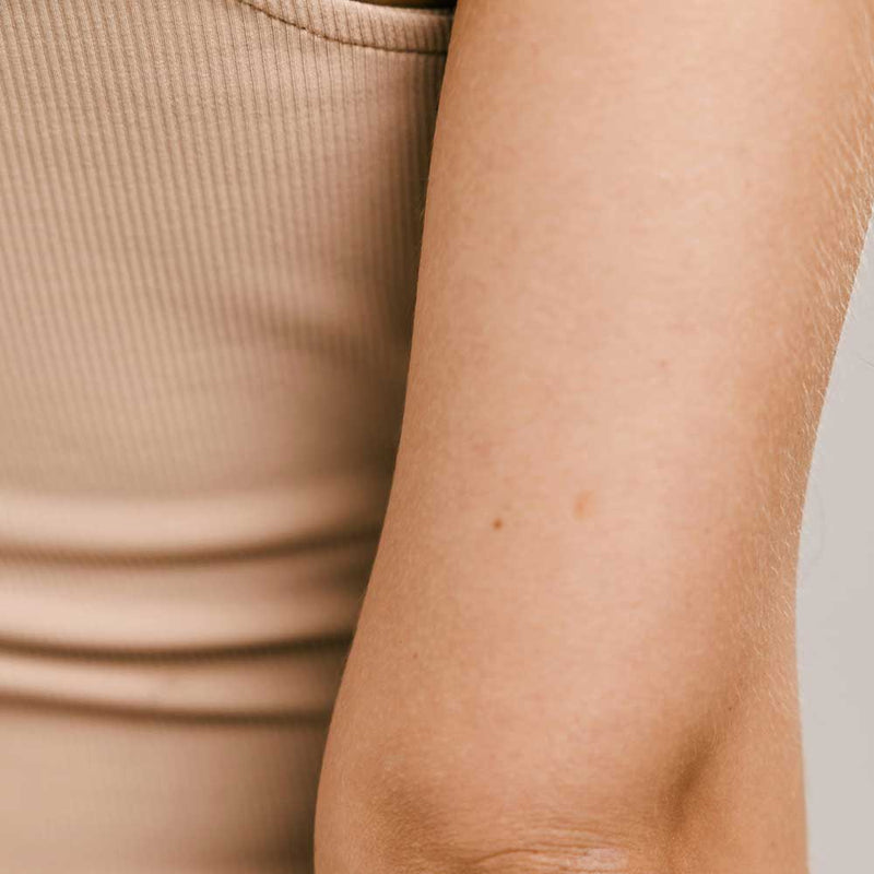 Close-up of the back of a woman's upper arm in a beige ribbed tank top, where keratosis pilaris usually shows up