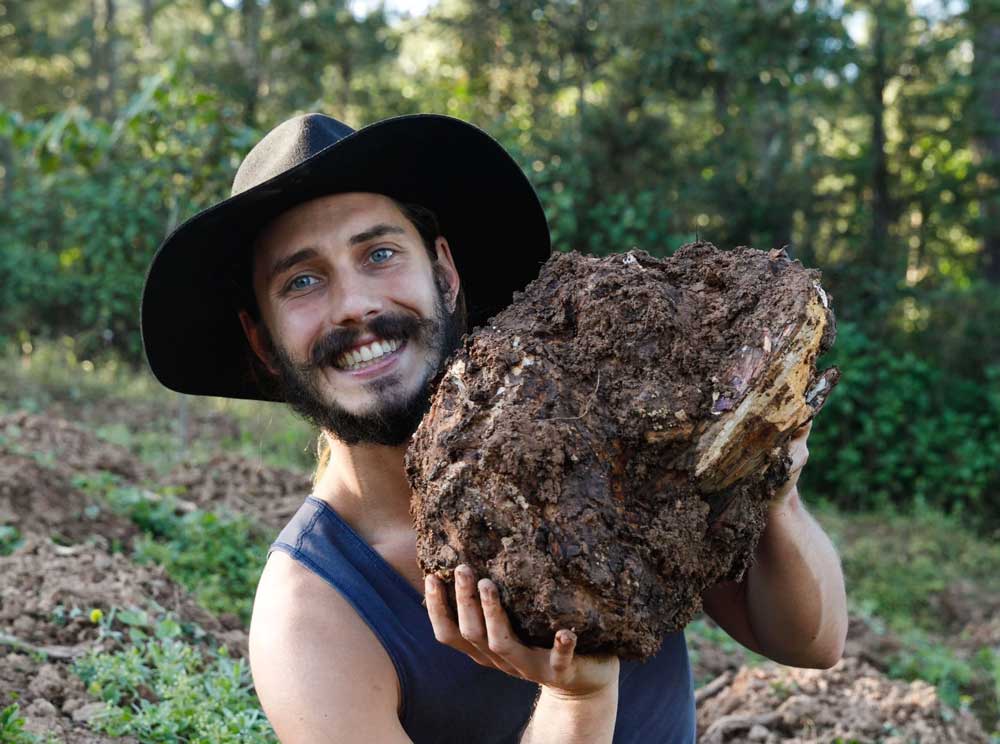 SuperFeast founder Mason Taylor in a black hat, smiling and holding a large tree mushroom outdoors