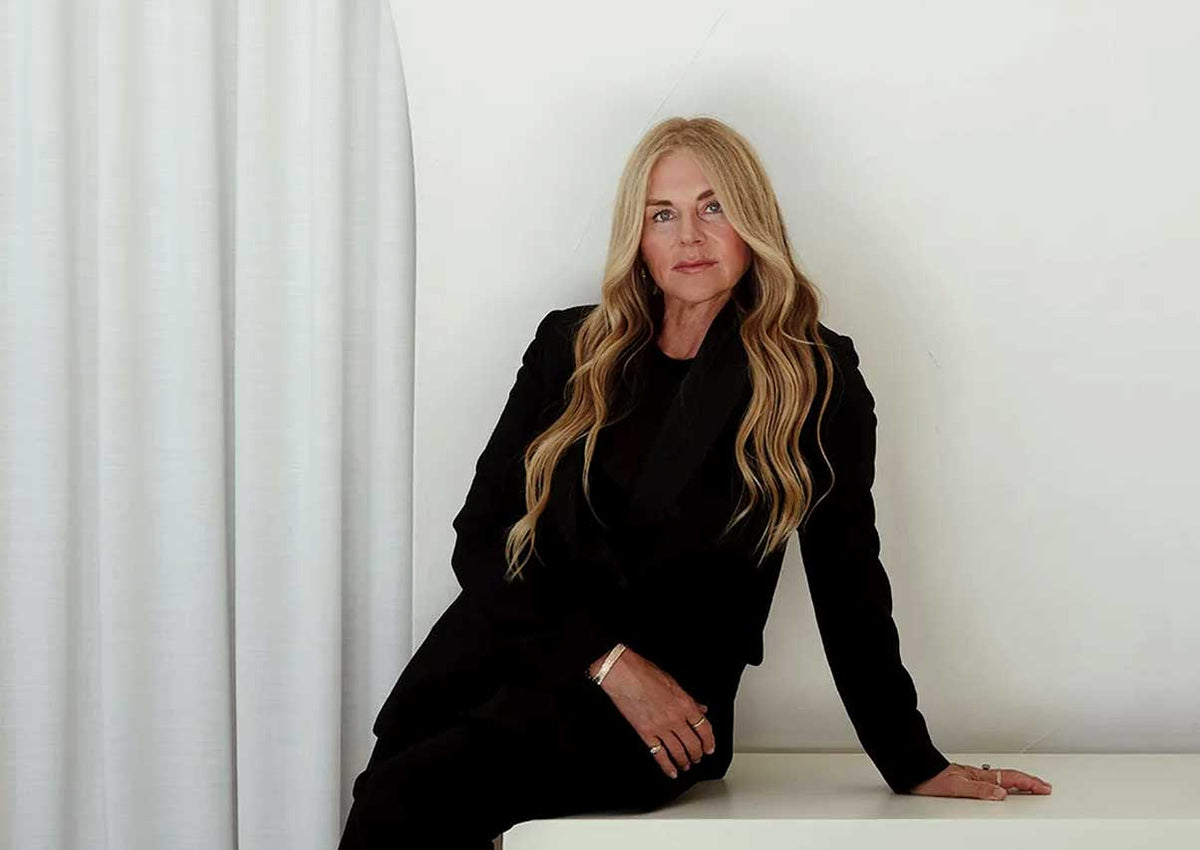 Mukti, founder of Mukti Organics, wearing black and leaning on a white table in front of a white wall
