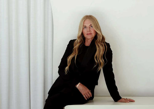 Mukti, founder of Mukti Organics, wearing black and leaning on a white table in front of a white wall