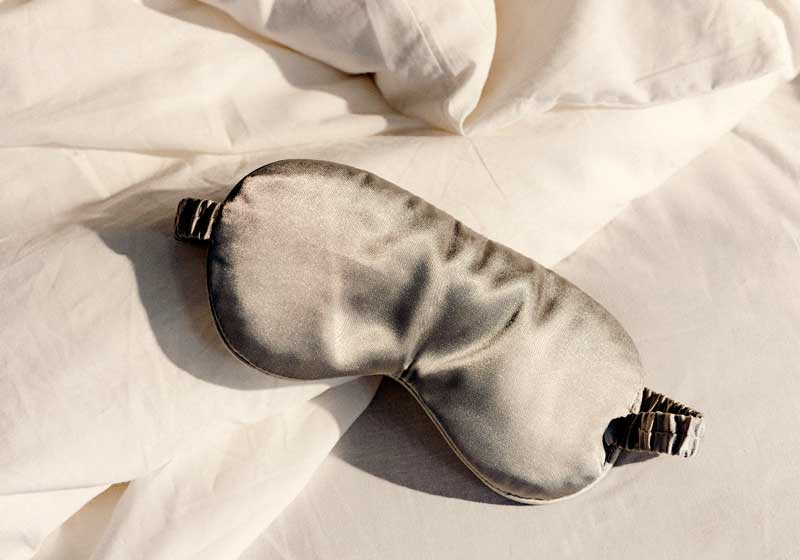 Charcoal coloured silk eye mask on white bed sheets
