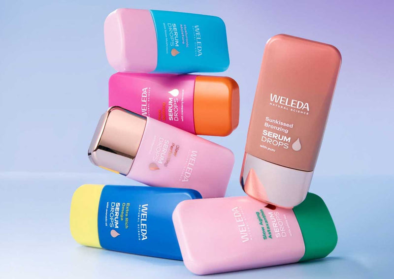 Weleda Serum Drops bottles stacked on a pale blue background in blue, pink, orange, yellow, terracotta and green