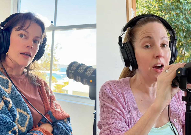 Matilda Brown in headphones and a blue patterned cardigan listening as Irene Falcone in a pink cardigan talks into a podcast microphone in the bright studio