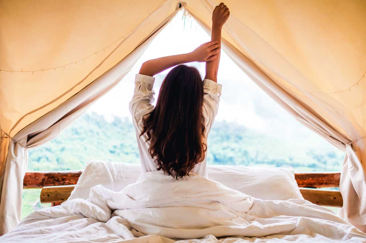 Woman waking up in bed well rested looking out a window into nature