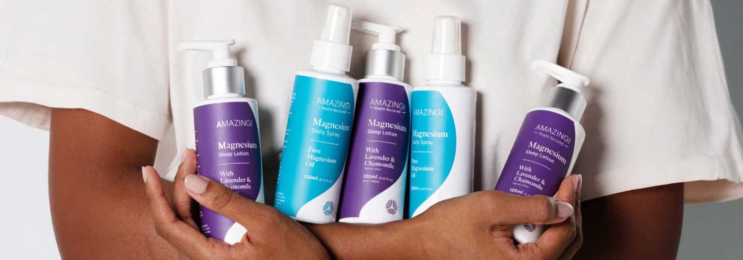 A person holds five bottles of Amazing Oils magnesium products, including Sleep Lotion and Daily Sprays, with purple and blue labels, against their chest.
