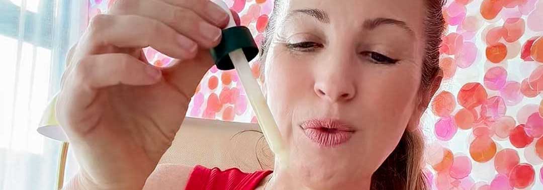 A woman holds a dropper with a liquid, appearing ready to use it, with colorful circular patterns in the background.