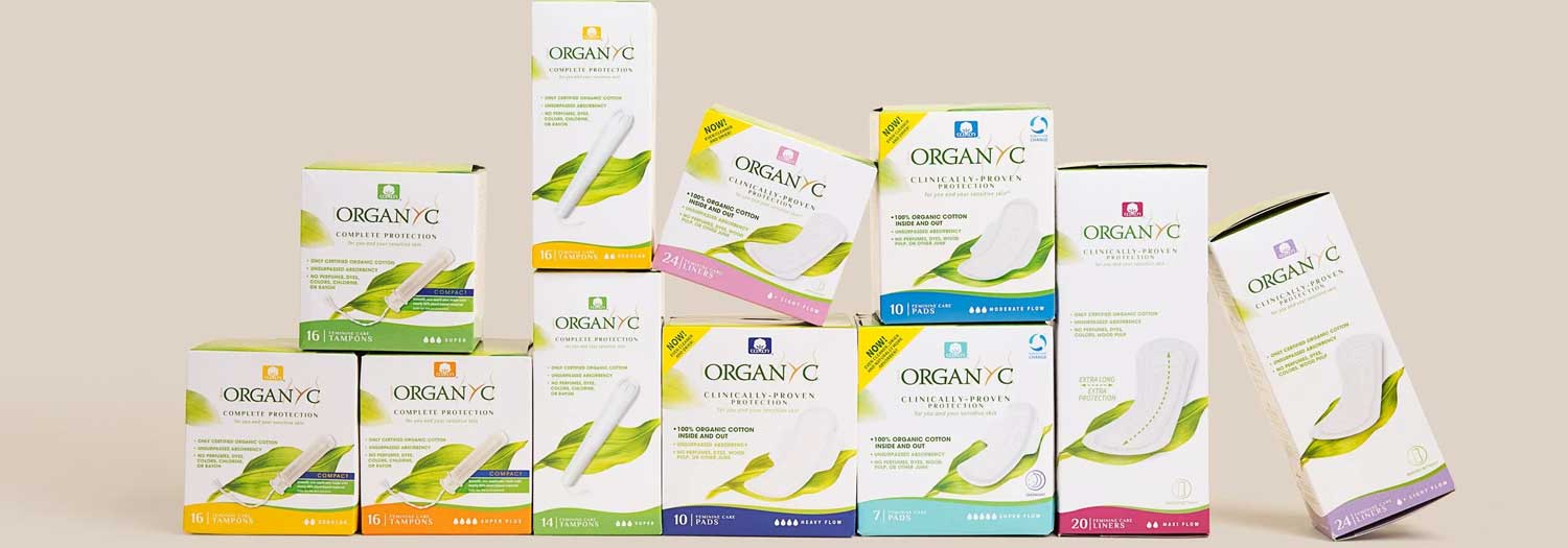Assorted boxes of Organyc brand feminine hygiene products, including pads and tampons, arranged in two rows against a neutral background. The packaging features green and white designs.