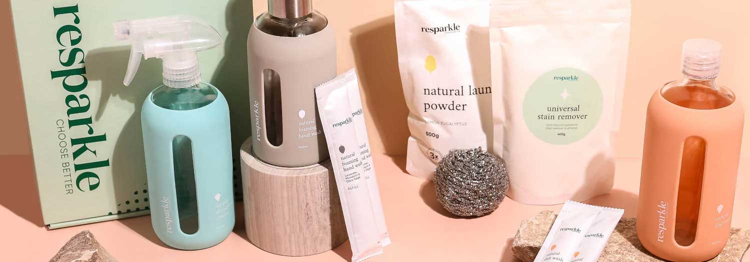 A collection of Resparkle eco-friendly cleaning products, including spray bottles, refill sachets, a metal scrubber, and powder packets, arranged neatly on a pastel surface.