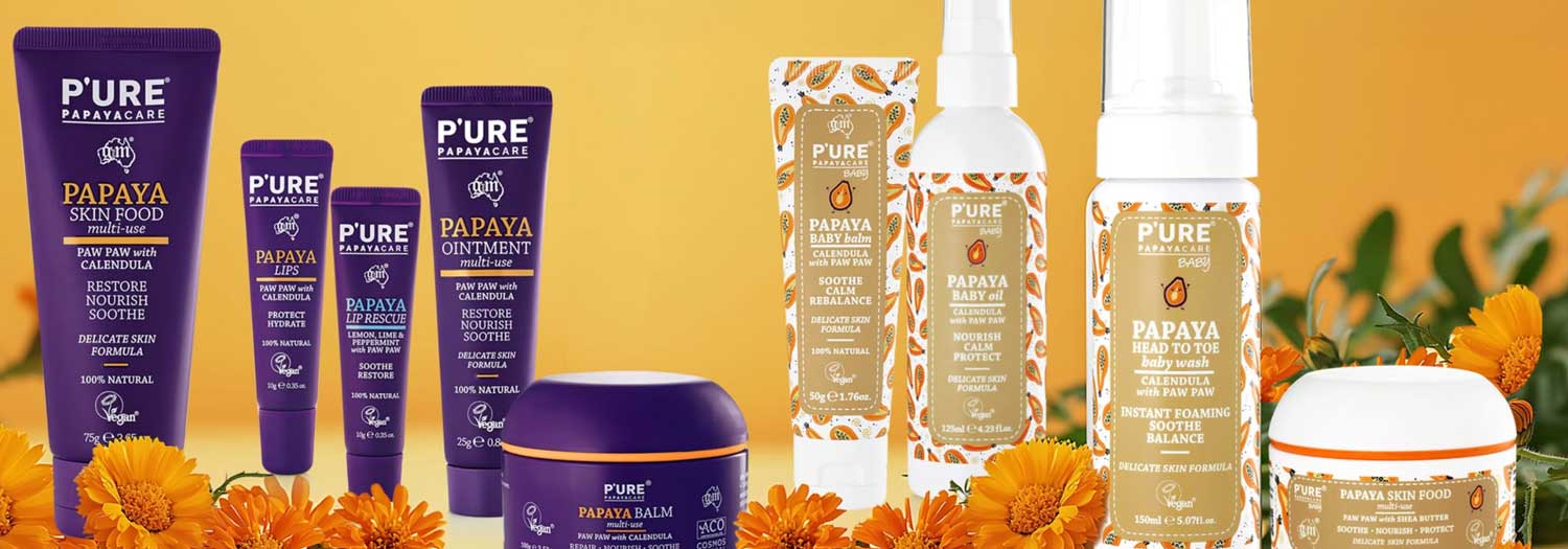A range of PURE Papayacare skincare products with purple and white packaging, displayed alongside vibrant orange calendula flowers against an orange background.