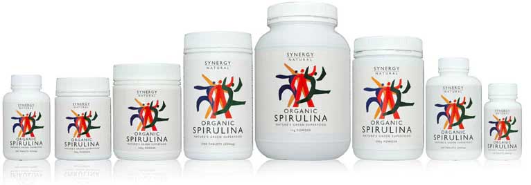 Eight bottles of Synergy Natural Organic Spirulina supplements in varying sizes, all with white labels featuring a colorful abstract design and the product name visible.