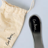 Ere Perez Steel Face Tool gua sha with its calico drawstring pouch on a white background