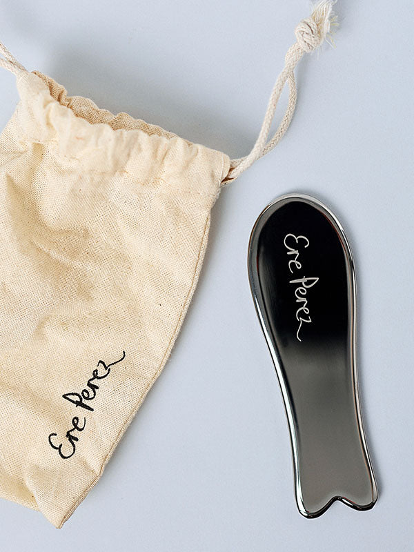 Ere Perez Steel Face Tool gua sha with its calico drawstring pouch on a white background