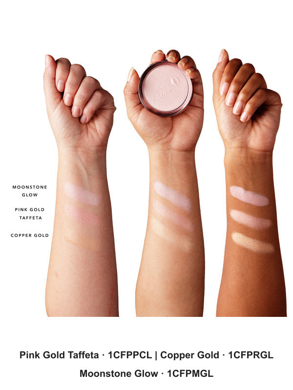 Three forearms with light, medium and dark skin show Gemmed Luminiser swatches. From wrist towards elbow: Moonstone Glow, pearly pink; Pink Gold Taffeta, rosy gold; Copper Gold, warm gold. The middle hand holds a compact. Shade codes: Moonstone Glow 1CFPMGL, Pink Gold Taffeta 1CFPPCL, Copper Gold 1CFPRGL.