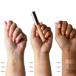 Three arms with varied skin tones each display four swatches of 100% Pure Fruit Pigmented® 2nd Skin Concealer 5ml, showing its natural finish and medium-full coverage. The middle hand holds a concealer tube on a white background.