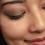 Close-up of a person’s face with smooth skin, winged eyeliner, long dark lashes, defined brows, and soft smile. Brown eyeshadow is from the 100% Pure Fruit Pigmented® Better Naked Palette 9g by 100% Pure.