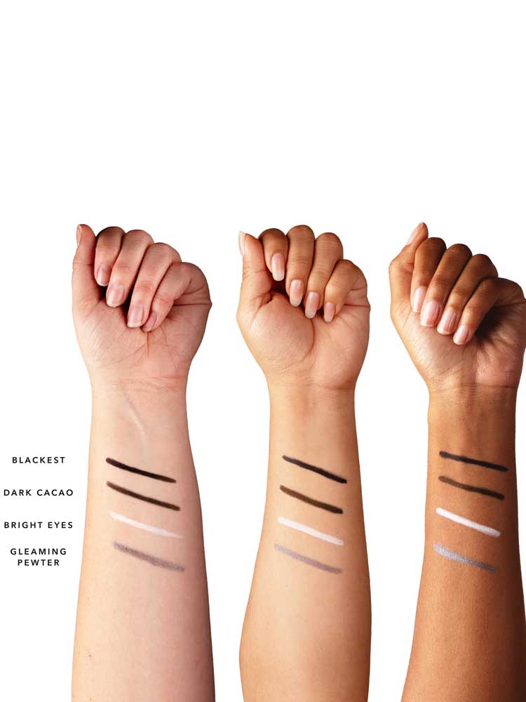 Three forearms with different skin tones show swatches of 100% Pure Creamy Long Last Eye Liner (1.14g) in Blackest, Dark Cacao, Bright Eyes, and Gleaming Pewter, highlighting how each long-lasting shade appears on varying skin tones.