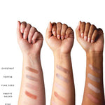 Three forearms of varied skin tones display five swatches from the 100% Pure 100% Fruit Pigmented® Pretty Naked Palette, showing Chestnut, Toffee, Flax Seed, Pretty Naked, and Pink Champagne shades flattering every complexion.