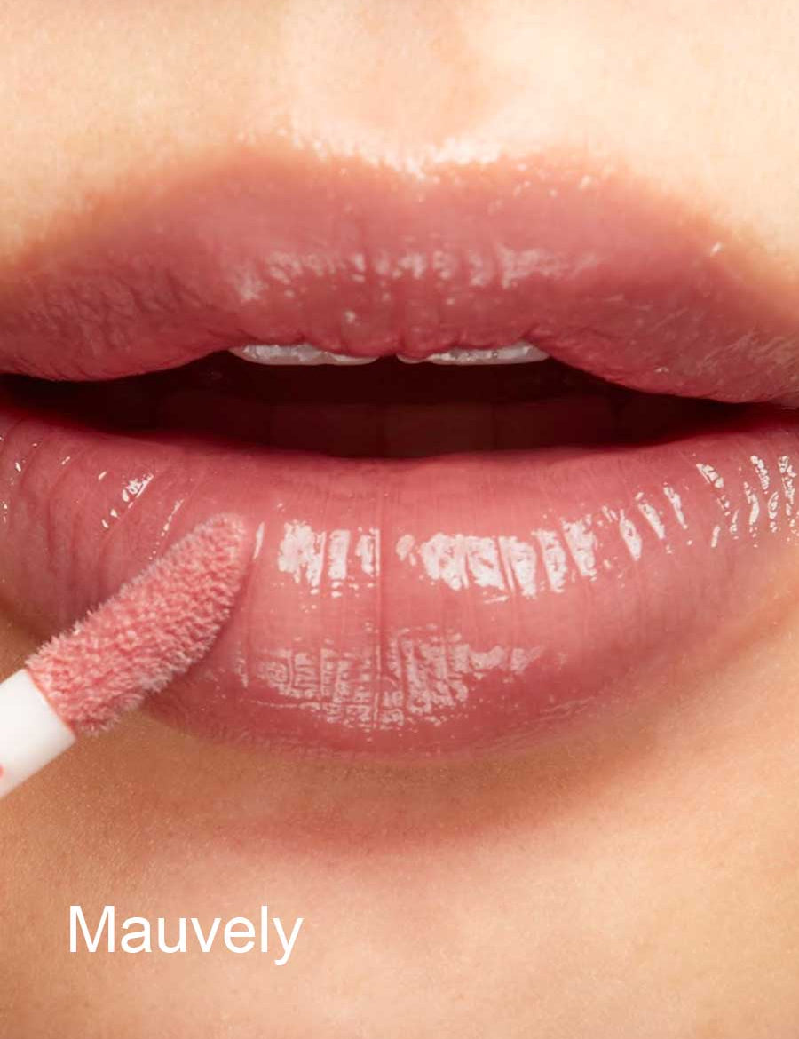 A close-up of lips being applied with 100% Pure Lip Gloss using a wand. Infused with vitamin E for hydration, the lips appear glossy and moisturized. The word Mauvely is in white at the bottom left corner.