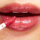 Close-up of glossy lips as a person applies 100% Pure Lip Gloss enriched with pomegranate oil using a wand applicator. The words Pomegranate Wine are written at the bottom of the image.