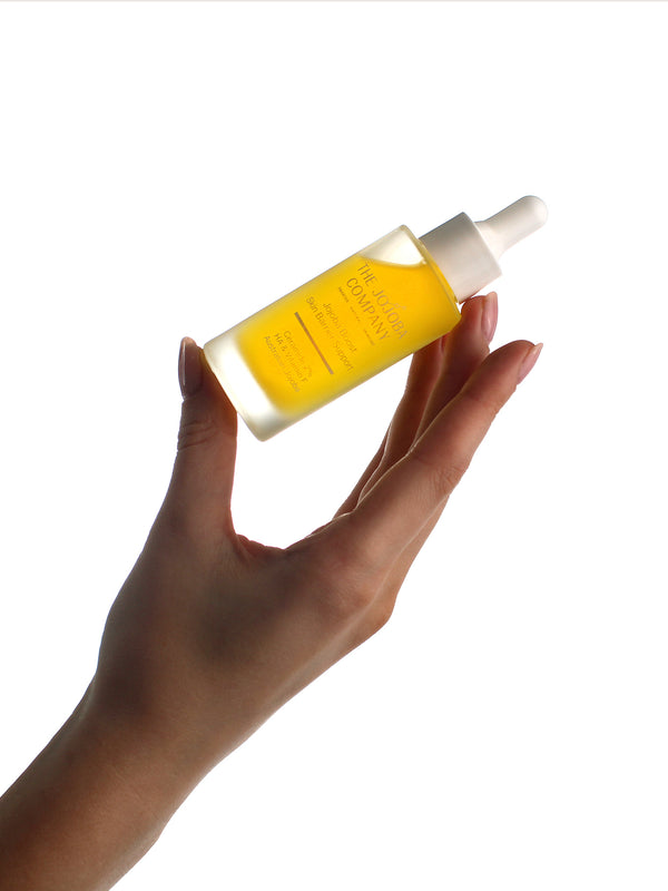 Hand holding a bottle of The Jojoba Company Jojoba Boost Skin Barrier Support