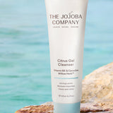 The Jojoba Company Citrus Gel Cleanser tube on a rock by the water