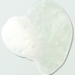 Close-up of a clear Coconut Shower Gel swatch on a pale mint surface. Its irregular outline surrounds fine bubbles and a foamy white patch concentrated on the left.