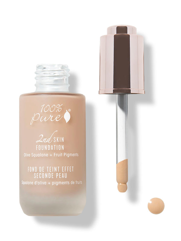 An open frosted bottle of golden-beige 100% Pure 2nd Skin Serum Foundation stands beside its rose-gold dropper cap. The exposed glass pipette holds foundation at the tip, above a small round drop.