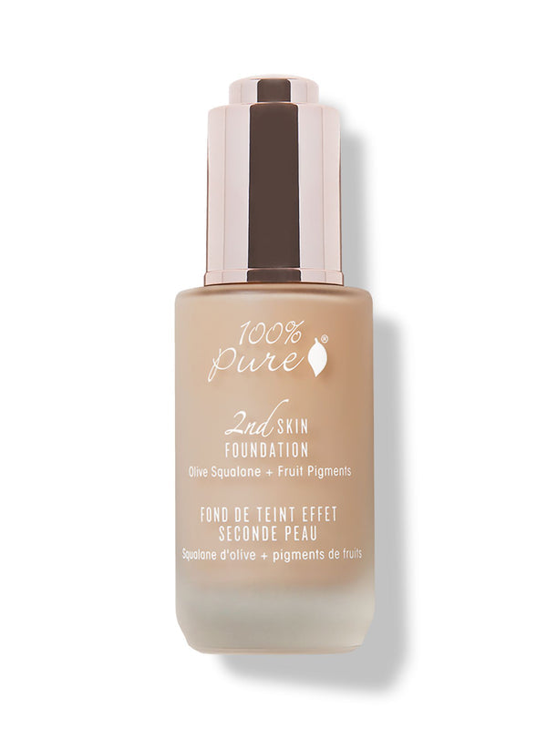 A closed frosted glass bottle of peach-beige 100% Pure 2nd Skin Serum Foundation has white lettering and a tall reflective rose-gold dropper cap. It casts a soft shadow to the right.
