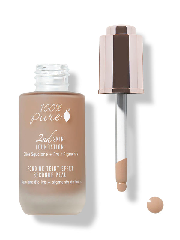 An open frosted bottle of tan 100% Pure 2nd Skin Serum Foundation stands beside its rose-gold dropper. Tan liquid coats the pipette tip, with a small round drop beneath it.