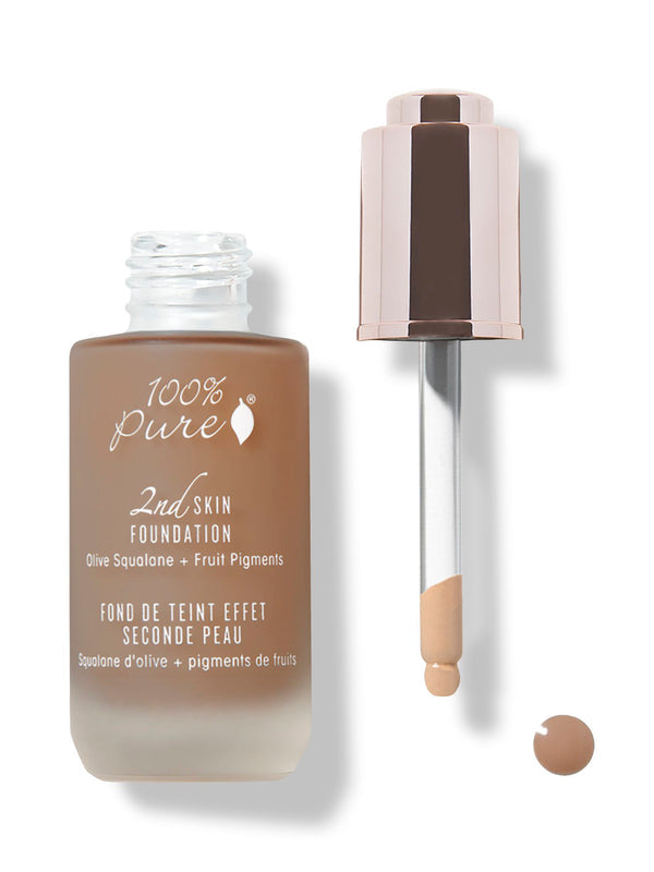An open frosted bottle of brown 100% Pure 2nd Skin Serum Foundation stands beside its rose-gold dropper. The pipette tip is coated with foundation, with a small brown drop below it.