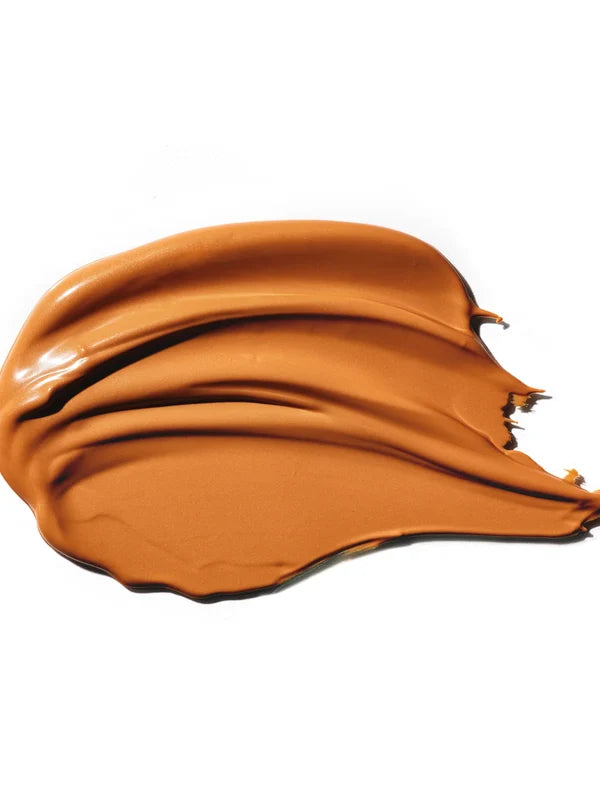 A thick caramel-brown swatch of 100% Pure BB Cream is spread into broad glossy folds. Raised curved ridges run across the surface, tapering toward the right.