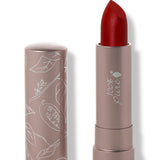 100% Pure Blood Orange matte lipstick with a slanted deep warm red tip extended from a taupe tube; its matching cap stands beside it with white botanical line drawings.