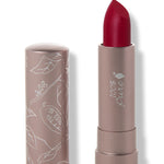 100% Pure Currant matte lipstick with a slanted deep crimson red tip extended from a taupe tube; its matching cap stands beside it with white botanical line drawings.