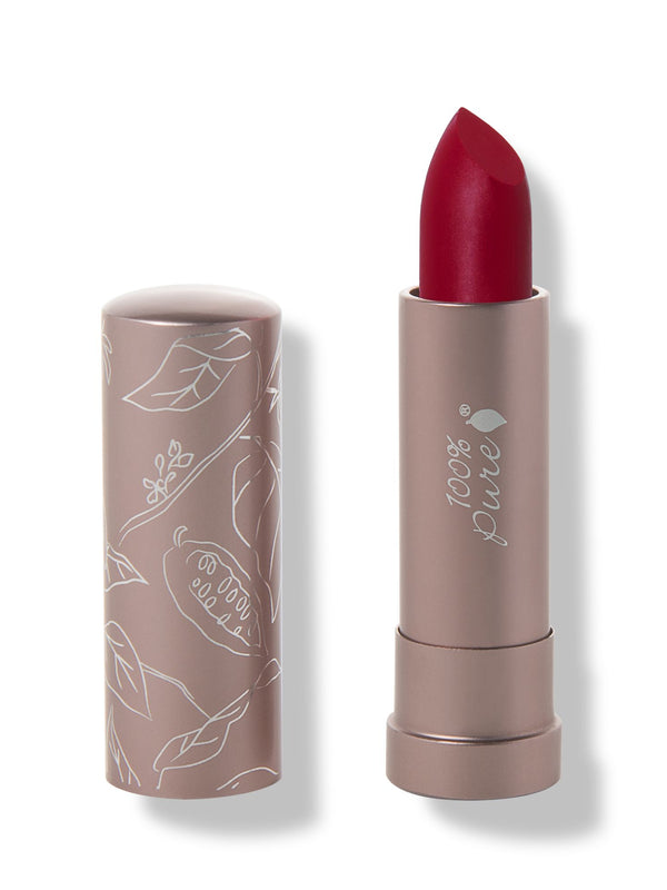 100% Pure Currant matte lipstick with a slanted deep crimson red tip extended from a taupe tube; its matching cap stands beside it with white botanical line drawings.