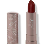 100% Pure Desert Rose matte lipstick with a slanted dark burgundy red tip extended from a taupe tube; its matching cap stands beside it with white botanical line drawings.