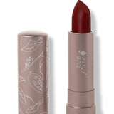 100% Pure Desert Rose matte lipstick with a slanted dark burgundy red tip extended from a taupe tube; its matching cap stands beside it with white botanical line drawings.