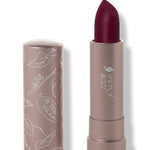 100% Pure Oasis matte lipstick with a slanted dark plum red tip extended from a taupe tube; its matching cap stands beside it with white botanical line drawings.