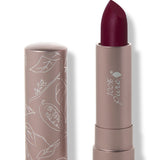 100% Pure Oasis matte lipstick with a slanted dark plum red tip extended from a taupe tube; its matching cap stands beside it with white botanical line drawings.