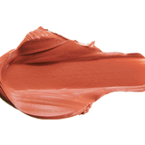 A warm peach-rose lipstick swatch is spread into a thick horizontal smear. Raised folds gather along its upper edge, while the centre is broad and smooth, with fine streaks along the lower edge.