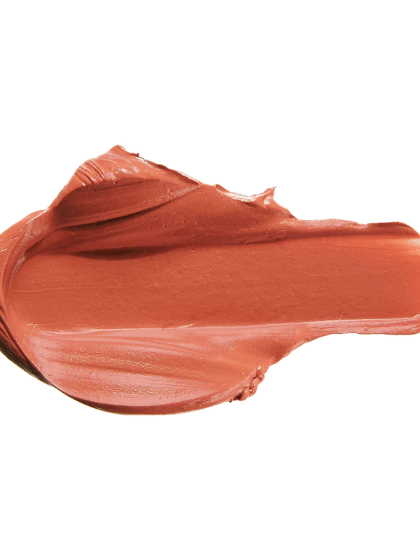 A warm peach-rose lipstick swatch is spread into a thick horizontal smear. Raised folds gather along its upper edge, while the centre is broad and smooth, with fine streaks along the lower edge.