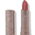 100% Pure Sahara matte lipstick with a slanted muted brick rose tip extended from a taupe tube; its matching cap stands beside it with white botanical line drawings.