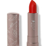 100% Pure Sonora matte lipstick with a slanted bright scarlet red tip extended from a taupe tube; its matching cap stands beside it with white botanical line drawings.