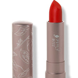 100% Pure Sonora matte lipstick with a slanted bright scarlet red tip extended from a taupe tube; its matching cap stands beside it with white botanical line drawings.