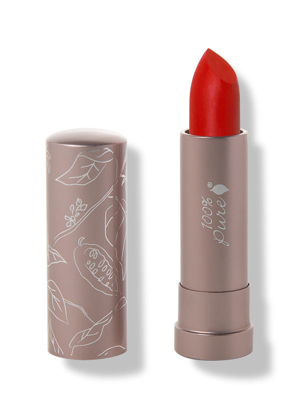 100% Pure Sonora matte lipstick with a slanted bright scarlet red tip extended from a taupe tube; its matching cap stands beside it with white botanical line drawings.
