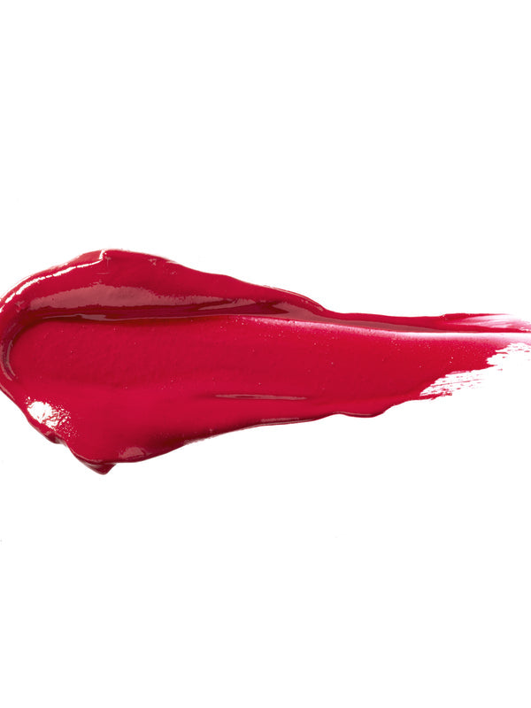 Cherry Cordial 100% Pure Lip Caramel swatch: thick, glossy bright berry-red liquid lipstick spread into an elongated smear, with raised ridges and a tapering streak at one end.