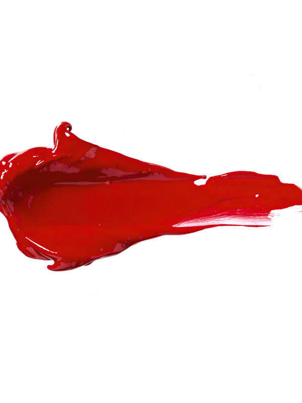 Red Velvet 100% Pure Lip Caramel swatch: thick, glossy rich red liquid lipstick spread into an elongated smear, with raised ridges and a tapering streak at one end.