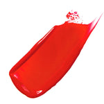 Scotch Kiss 100% Pure Lip Caramel swatch: a broad, glossy orange-red stroke spread diagonally, with a smooth centre and a tapered, streaked edge.
