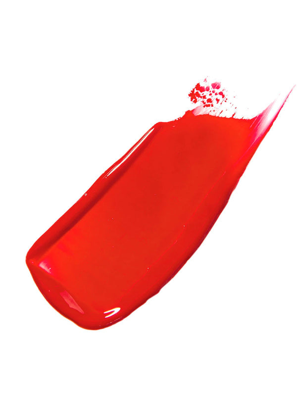 Scotch Kiss 100% Pure Lip Caramel swatch: a broad, glossy orange-red stroke spread diagonally, with a smooth centre and a tapered, streaked edge.