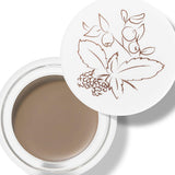 100% Pure Long Last Brows in Blonde: an open white pot filled with light taupe-brown brow cream. A fine drawing of leaves and berries decorates the white lid resting behind the pot.