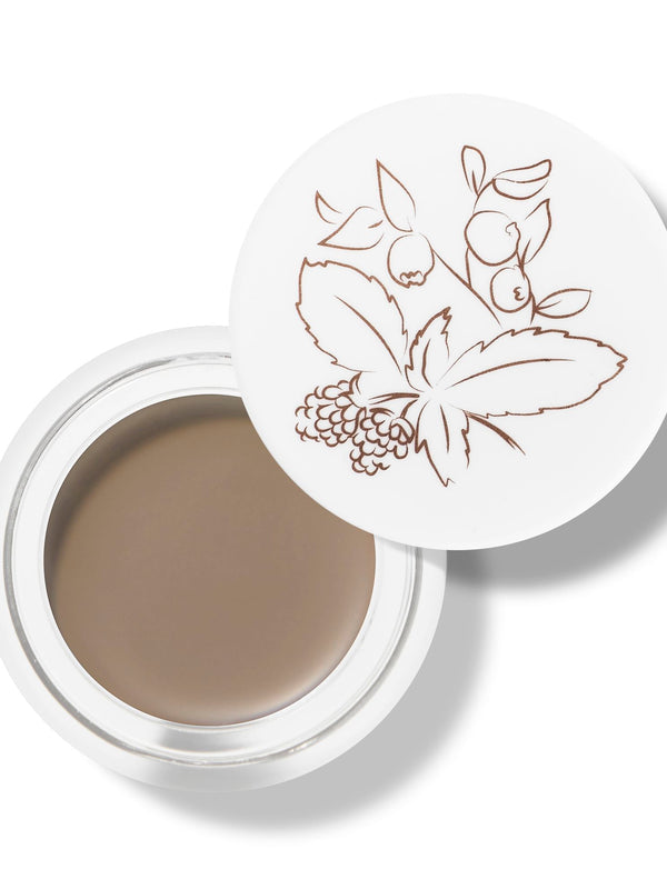 100% Pure Long Last Brows in Blonde: an open white pot filled with light taupe-brown brow cream. A fine drawing of leaves and berries decorates the white lid resting behind the pot.